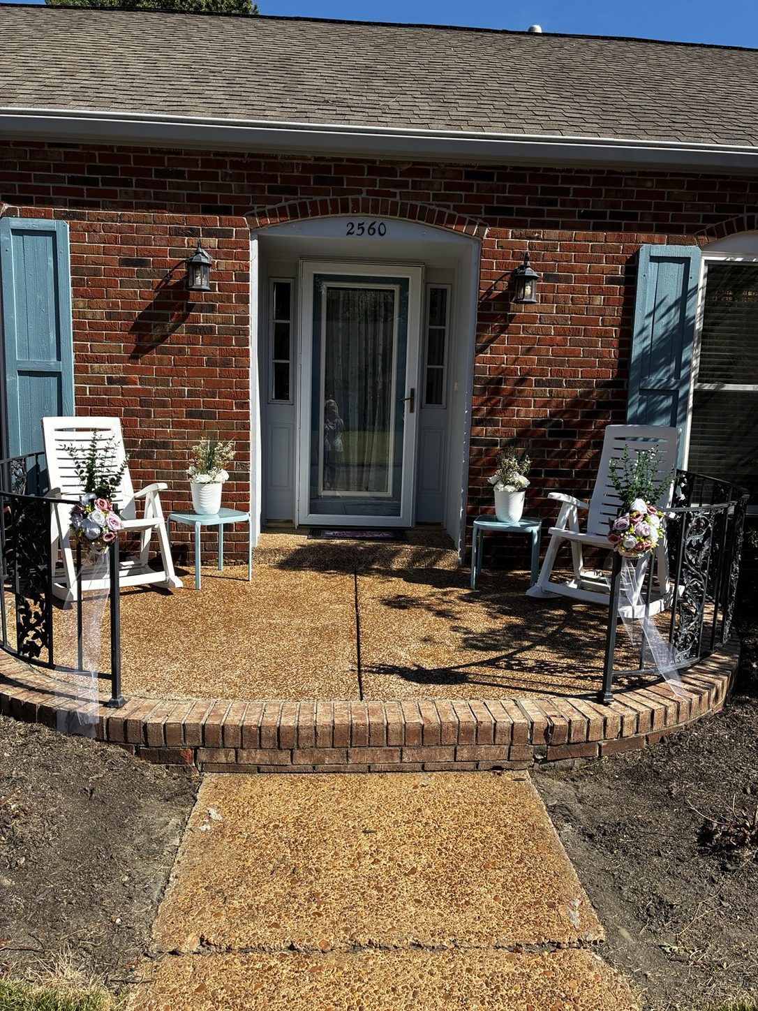 Front porch of the venue with white rocking chairs, white pots of flowers on small blue tables beside the door, and flower bouquets with white tulle on the iron railings